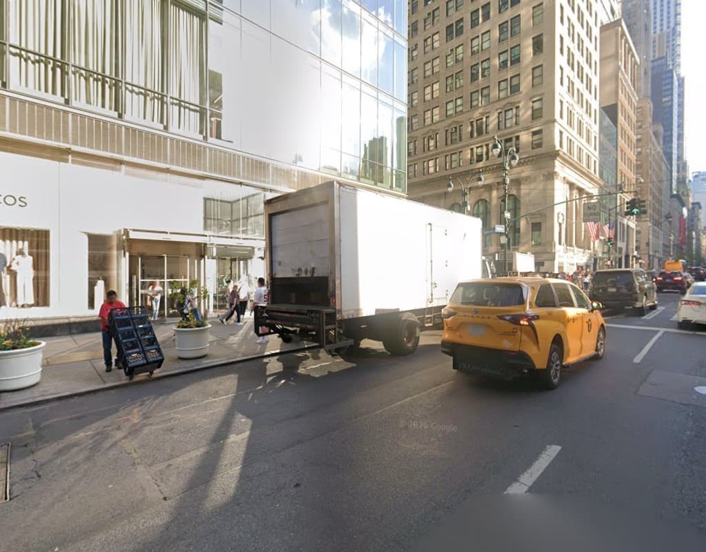 Google Street View image of Fifth Avenue in New York, with buildings, a delivery truck, a yellow taxi and pedestrians