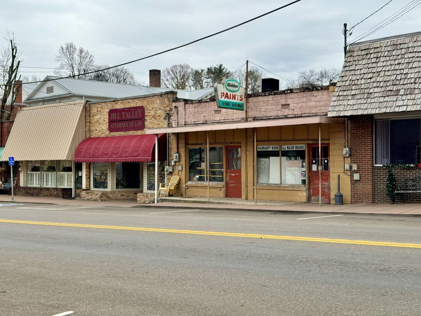 A small-town main street with shopfronts, painted fascia signs, an awning, glazed windows and an empty carriageway