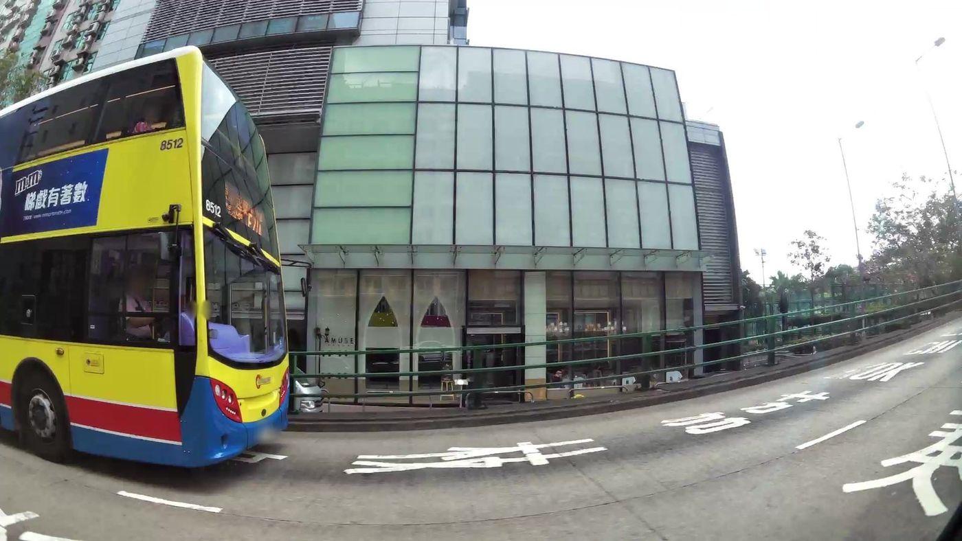 Wide-angle street-level frame of a Hong Kong road, with a double-decker bus, a glazed building frontage, lane markings and street lighting